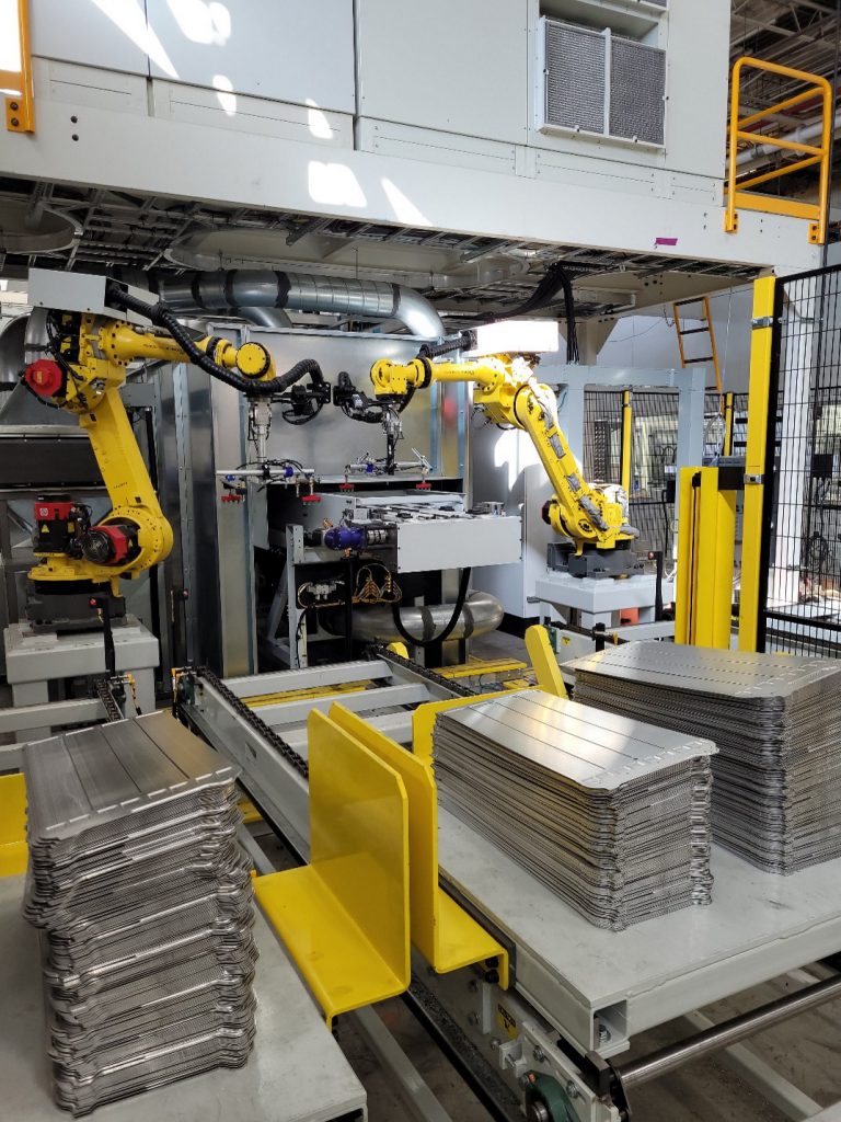 Two yellow Fanuc robots picking parts up coming out of a stamping press and playing them on conveyors in a Linear Automation end-of-line cell.