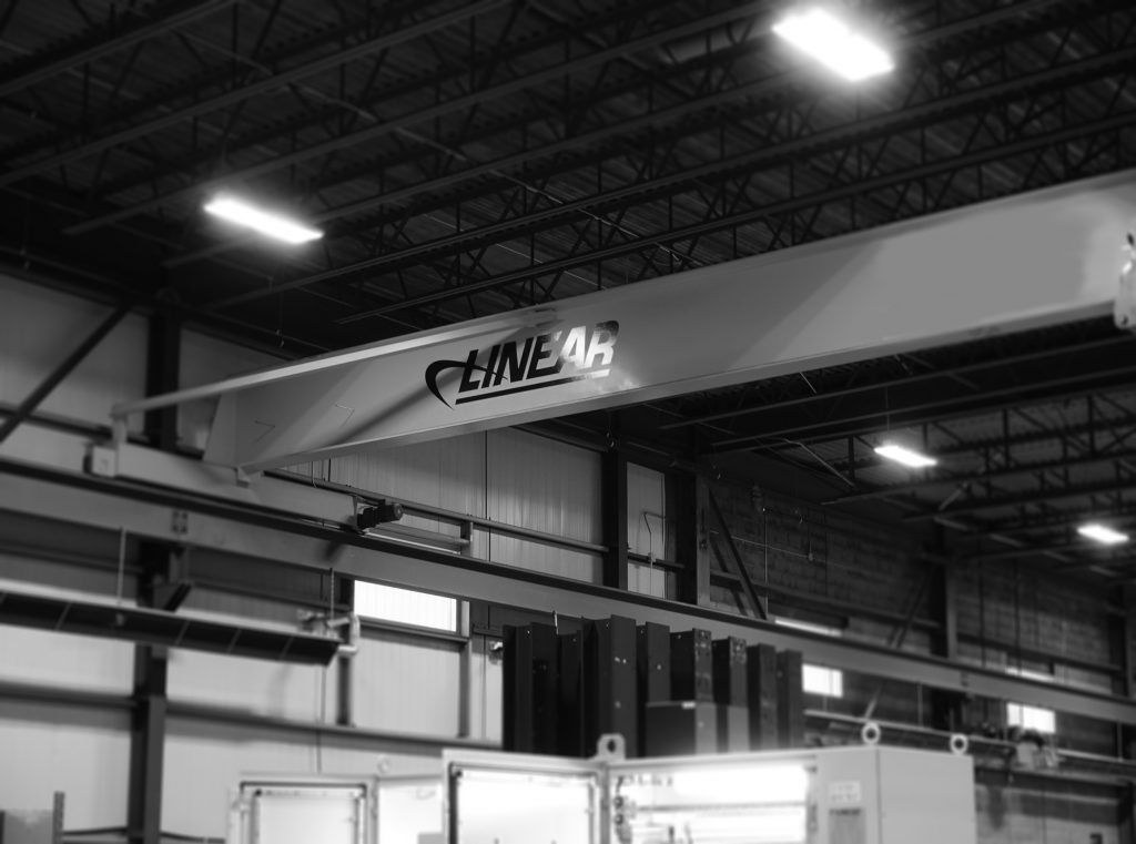 A black and white image of a Linear Automation logo on the bar of a large shop crane.