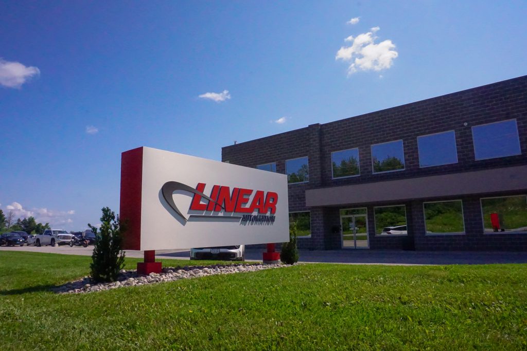 An image of a Linear Automation sign outside of the Barrie Headquarters, with green grass and blue sky.