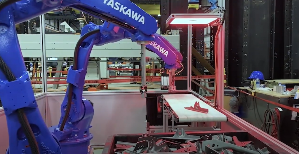 An image of two blue Yaskawa robots being used in a Linear Automation bin-picking system, with one picking the part out of a bin and placing it on a conveyor, and another picking up the same part and putting it onto a slide, that positions and drops the part into a new bin.